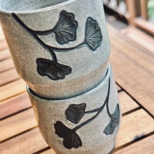 set of two handmade ceramic cups decorated with a speckled gray glaze and dark brown ginkgo carvings