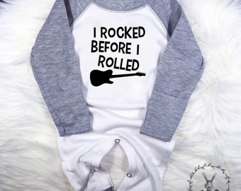 Może przedstawiać: Biały śpioszek dla niemowlęcia z szarymi rękawami. Śpioszek ma czarny wzór gitary i napis "I rocked before I rolled".