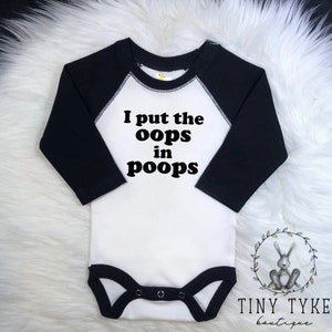 May include: White baby onesie with black raglan sleeves. The onesie has black text that reads "I put the oops in poops".