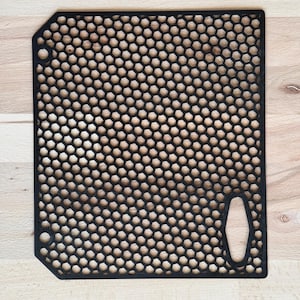 Könnte beinhalten: Schwarzes Kunststoff-Gitterpaneel mit hexagonalem Muster und einem ausgeschnittenen Griff. Das Paneel hat eine abgerundete Kante und zwei kleine Löcher auf der linken Seite.