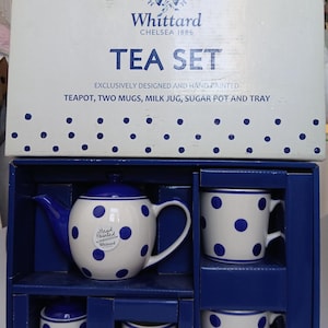 May include: A hand-painted tea set by Whittard of Chelsea, featuring a white and blue polka dot design. The set includes a teapot, two mugs, a milk jug, a sugar pot, and a tray. The box is white with blue polka dots.