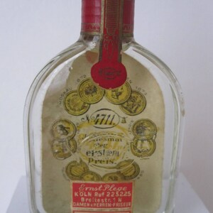 May include: A clear glass bottle with a red and gold label. The label has the text "4711" and "desmai der erster Preis."  The bottle also has a smaller label with the text "Ernst Plege KOLN Ruf 223225 Breitestr. 1N DAMEN HERREN-FRISEUR".