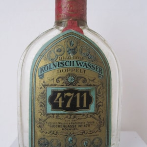 May include: A clear glass bottle with a gold and blue label. The label says "Blau Gold Kolnisch Wasser Doppel 4711" and "aus der K&ouml;lnisch Wasser & Parfumerie-Fabrik "Glockengasse N&deg; 4711" K&ouml;ln Ph."