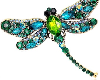 May include: A dragonfly brooch crafted from gold-tone metal and embellished with green, teal, and blue crystals. The body of the brooch is a large, bright green crystal. The wings are decorated with various sizes of crystals.