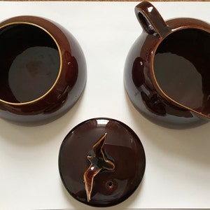 May include: A brown ceramic teapot with a bird design on the lid and a matching sugar bowl and creamer.