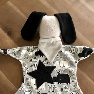 May include: A gray and white baby security blanket with a black star and a black and white animal print. The blanket has a sewn-on gray and white dog head with black ears and pink stitching for the eyes and nose.