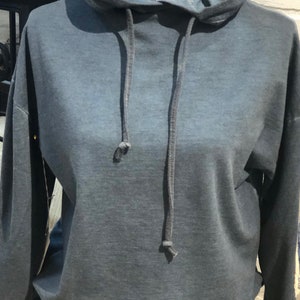 Puede incluir: Una sudadera con capucha gris oscuro con cordón. La sudadera tiene un efecto degradado descolorido, con un tono gris más claro en la parte superior y un tono más oscuro en la parte inferior.