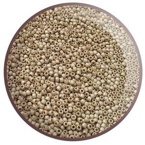 May include: A close-up view of a large quantity of small, round, beige seed beads. The beads are arranged in a circular pattern, creating a uniform and textured surface.