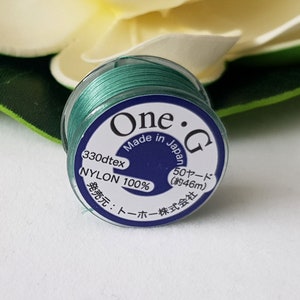 May include: A spool of teal nylon thread labelled "One.G Made in Japan 330dtex NYLON 100% 50ヤード (約46m) 発売元:トーホー株式会社"