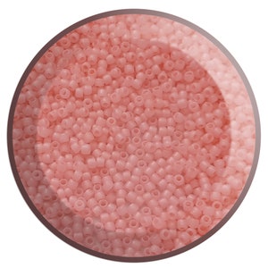 May include: A close-up view of a bowl filled with small, opaque, light pink seed beads.