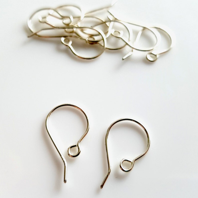 May include: Silver earring hooks, a close-up of two earring hooks, silver in color, on a white background.