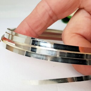 May include: A close-up of three silver metal strips, rolled into a circle, with a shiny, reflective surface.