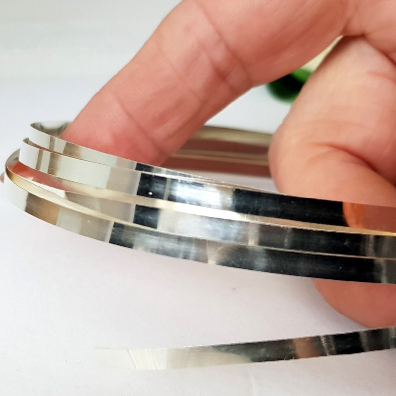 May include: A close-up of three silver metal strips, rolled into a circle, with a shiny, reflective surface.