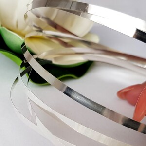 May include: Close-up of three silver metal strips, stacked on top of each other. The strips are shiny and reflective.