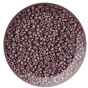 May include: A close-up view of a container filled with small, round, purple beads. The beads have a slight iridescent sheen.