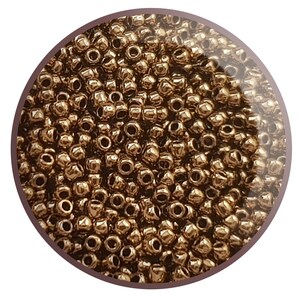 May include: A close-up image of a large quantity of small, round, metallic gold beads. The beads are arranged in a circular pattern, creating a uniform, textured surface.