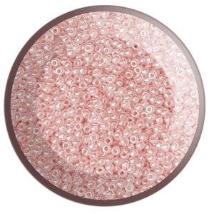 May include: A close-up view of a container filled with small, round, light pink seed beads. The beads have a slight iridescent sheen.