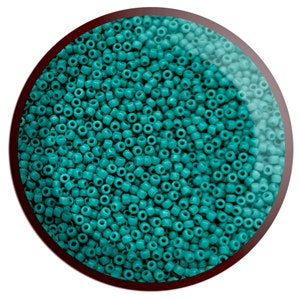 May include: A close-up view of a large quantity of teal blue seed beads. The beads are small and round, and they are arranged in a random pattern.
