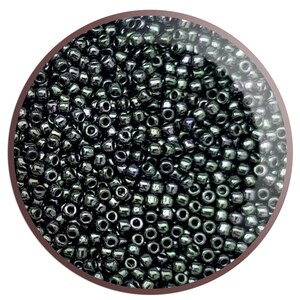 May include: A close-up image of a large quantity of small, round, black seed beads. The beads have a slight iridescent sheen.