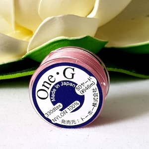 May include: A spool of pink nylon thread labelled "One G Made in Japan 330dtex NYLON 100% 50 yards (approx. 46m)  発売元: トーホー株式会社"