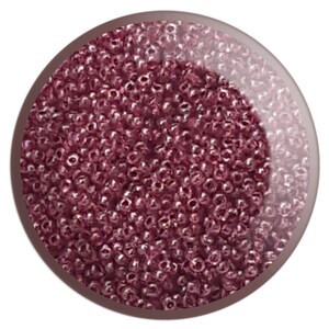 May include: A close-up image of a large quantity of small, round, iridescent pink beads. The beads are arranged in a random pattern and appear to be made of glass.