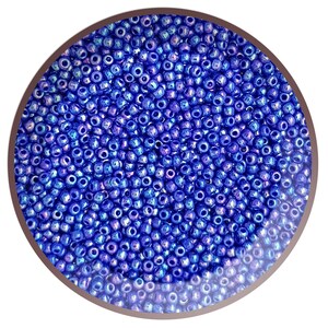 May include: A close-up image of a large quantity of small, round, blue seed beads. The beads have a metallic sheen and are arranged in a circular pattern.