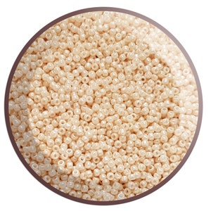 May include: A close-up view of a large quantity of small, round, cream-coloured beads. The beads have a slight iridescent sheen.