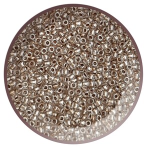 May include: A close-up view of a large quantity of small, silver-coloured seed beads. The beads are round and have a smooth, shiny finish.