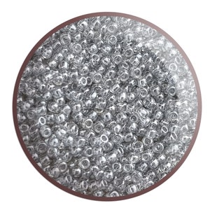 May include: A close-up view of a large quantity of small, round, silver-coloured beads. The beads are arranged in a circular pattern and appear to be made of glass.