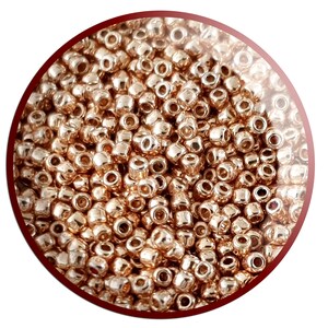 May include: A close-up image of a large quantity of small, round, gold-coloured beads. The beads have a shiny, metallic finish.