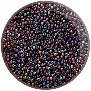 May include: A close-up image of a large quantity of small, round, iridescent beads. The beads are a mix of dark purple, brown, and blue colours.