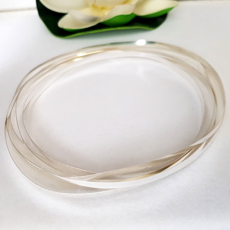 May include: A silver bangle bracelet with a twisted design. The bracelet is made of multiple strands of silver wire that are twisted together to create a unique and stylish look.