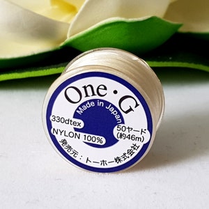 May include: A spool of off-white nylon thread with a blue and white label. The label reads "One G Made in Japan" and includes Japanese text. The spool contains approximately 46 meters of thread.
