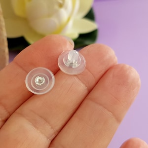 May include: Two clear plastic earring backs with a small silver post in the center. The backs are designed to fit over the post of an earring.