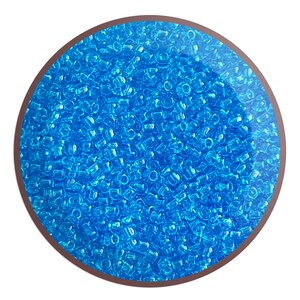May include: A close-up view of a large quantity of small, translucent blue plastic beads. The beads are arranged in a circular pattern and appear to be uniform in size and shape.