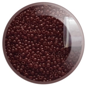 May include: A close-up image of a container filled with small, dark brown seed beads. The beads are round and have a smooth, glossy finish.