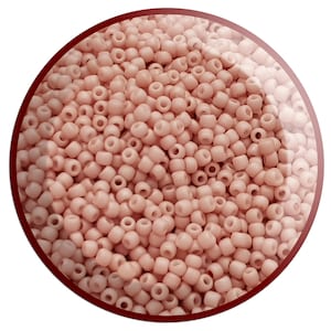 May include: A close-up of a collection of small, pale pink seed beads. The beads are consistent in size and shape, with a cylindrical form and a central hole. The beads are within a circular frame with a dark red border.