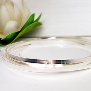 May include: A close-up of a silver wire, coiled into a circle. The wire is shiny and reflective, and the coils are neatly stacked on top of each other.