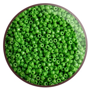 May include: A close-up image of a large quantity of small, round, green glass beads. The beads are all the same size and shape, and they are arranged in a random pattern.