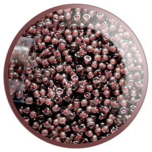 May include: A close-up of a container filled with small, round, iridescent purple beads. The beads have a metallic sheen and are arranged in a random pattern.
