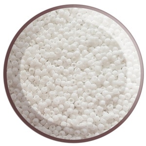 May include: A close-up of a circular container filled with many small, opaque white seed beads. The beads are uniform in size and shape, creating a dense, textured surface. The container has a brown border.