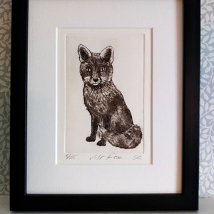 Puede incluir: Una impresión enmarcada en negro de un zorro en posición sentada. El zorro está dibujado en tonos grises y marrones. La impresión se titula "Wild Fox" y está numerada 9/25.