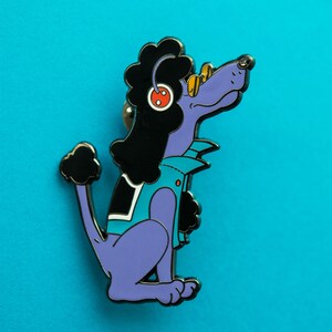 May include: Purple poodle with black fur wearing a turquoise jacket and sunglasses. The poodle has a red button on its ear and is sitting with its tail curled.