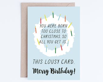 May include: A light blue greeting card with a brown envelope. The card has a wreath of colorful candles around the text "YOU WERE BORN TOO CLOSE TO CHRISTMAS. SO ALL YOU GET IS... THIS LOUSY CARD. Merry Birthday!"