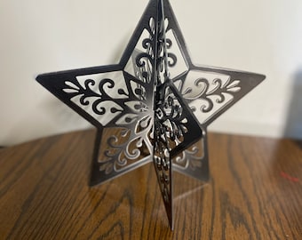 May include: A black, intricately designed, paper star ornament. The star is folded and has a 3D effect.
