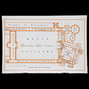 May include: A vintage map of the Vatican Museums in Rome, Italy. The map shows the layout of the museum, including the Braccio Nuovo, the Galleria dei Candelabri, the Giardino della Pigna, and the Cortile Ottagono al Belvedere. The map is printed in orange and black on a white background.