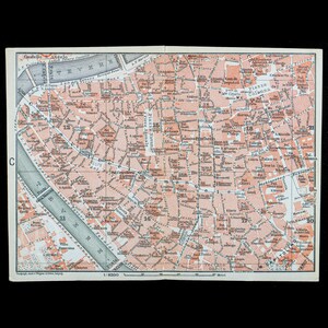 May include: A vintage printed map of Rome, Italy, featuring the Tiber River in grey and city streets in shades of peach and white. The map includes labeled landmarks like Piazza Navona, the Pantheon, and Castello S. Angelo with a 1:8300 scale.