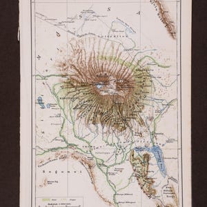 May include: An antique topographical map titled KILIMA-NDSCHARO, featuring detailed contour lines of the mountain in shades of brown, green, and blue. The map includes geographical labels, a scale, and a legend at the bottom left corner.