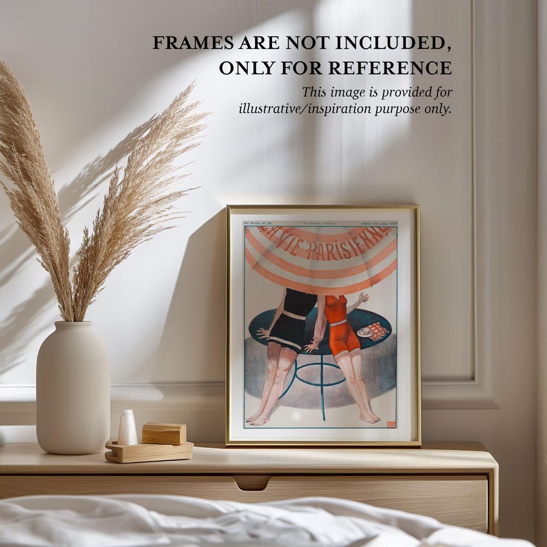 a framed vintage poster of two women in swimsuits, placed on a wooden dresser next to a vase with dried reeds.
