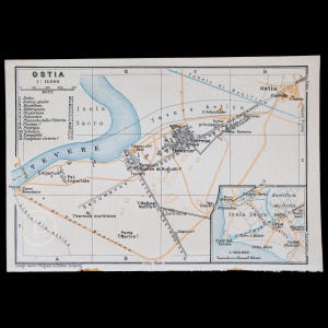 May include: A printed map of Ostia featuring a grid system, the Tevere river in blue, and various historical site labels. It includes a smaller inset map of the surrounding region, a scale bar in meters, and the text Geogr. Anst. v. Wagner & Debes, Leipzig.